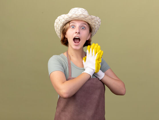 女兴奋的年轻斯拉夫女园丁戴着园艺帽和手套手牵手在橄榄绿上花园斯拉夫园艺