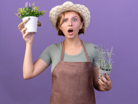 焦虑焦虑的年轻斯拉夫女园丁戴着园艺帽 手里拿着紫色花盆里的花年轻斯拉夫花园