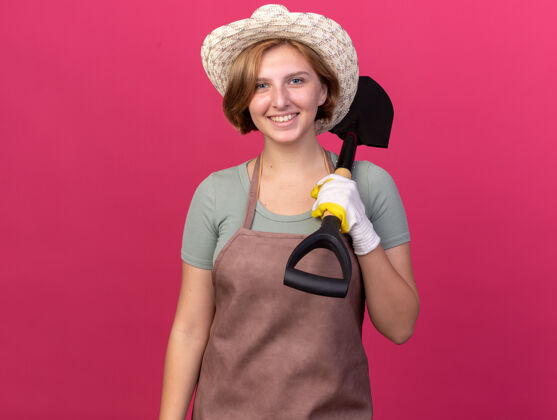 园艺微笑着的年轻的斯拉夫女园丁戴着园艺帽和手套 肩上扛着一把铁锹年轻黑桃斯拉夫