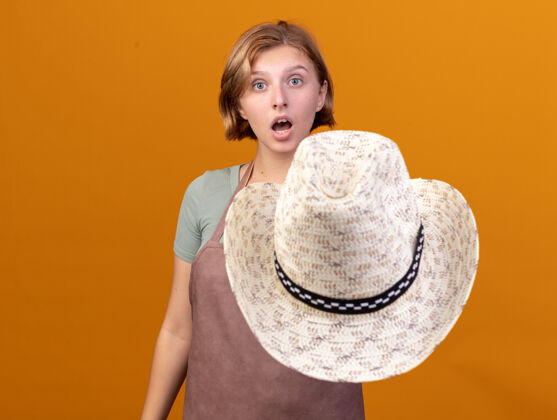 帽子令人印象深刻的年轻斯拉夫女园丁手持园艺帽 看着相机上的橙色年轻的印象园艺