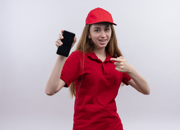 送货快乐的年轻送货女孩穿着红色制服 拿着手机指着与世隔绝的白色空间年轻红色快乐