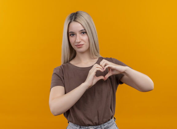 金发高兴的年轻金发女孩做心脏标志看孤立的橙色空间与复制空间女孩标志橙色