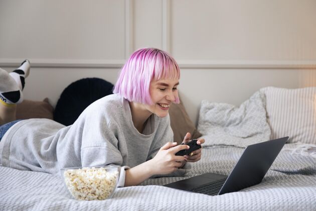 技术粉红色头发的女人在玩笔记本电脑上的操纵杆享受视频游戏乐趣