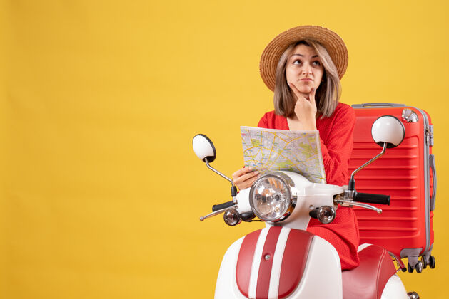 肖像困惑的年轻女士骑着轻便摩托车 手拿红色手提箱 手里拿着车票手提箱抱着人