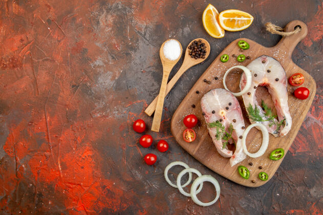 晚餐新鲜生鱼和胡椒洋葱绿色西红柿的顶视图在混合色表面左侧的木制砧板上容器左侧膳食