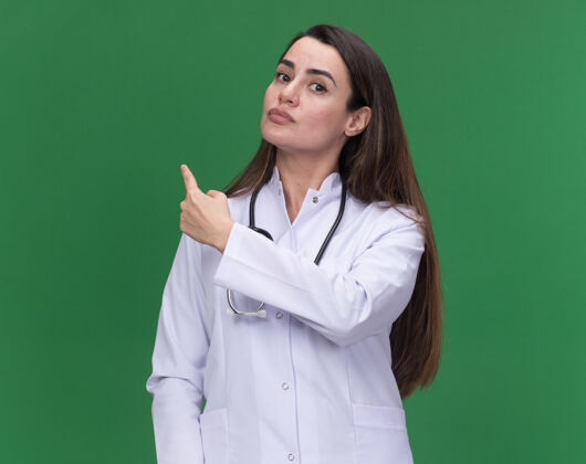 医生自信的年轻女医生穿着带听诊器的医用长袍点回绿色点年轻医疗