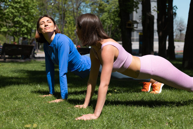 锻炼阳光明媚的日子里 两个穿着运动服的漂亮女人在公园的草地上锻炼植物 互相支撑着快乐的情绪健康朋友健身