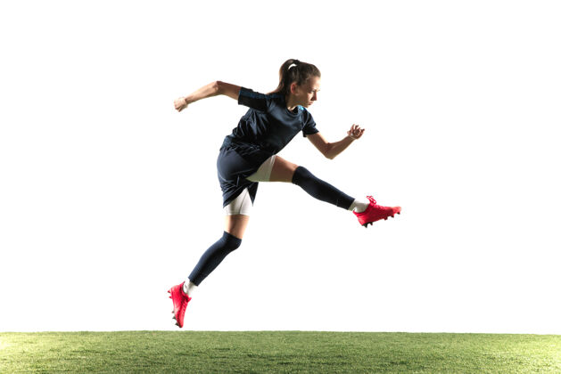 姿势年轻的女足球运动员或足球运动员 长发 运动服和靴子 为目标踢球 跳跃 白色背景健康的生活方式 职业体育 爱好的概念女衣服运动员