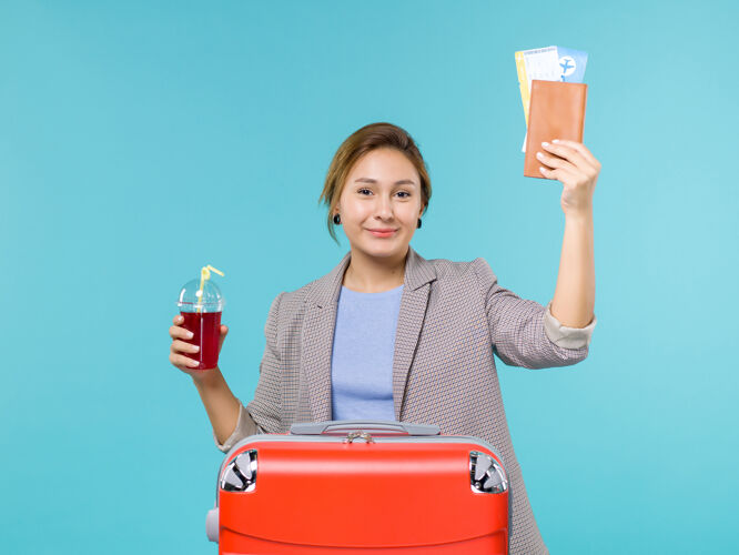 假期正面图：度假中的女性手持新鲜的樱桃汁和蓝色背景上的机票旅行旅行飞机度假旅行票人女人