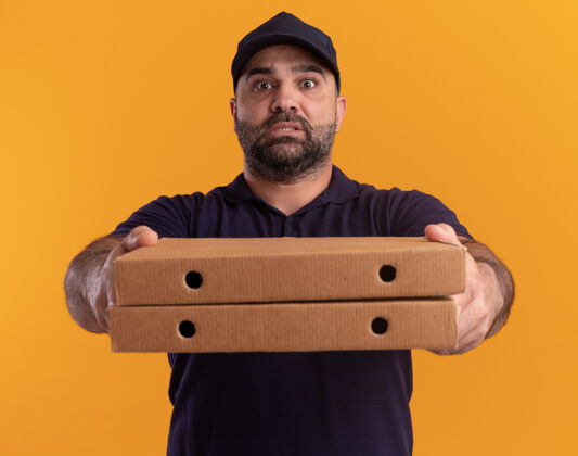 脸一个穿着制服 戴着帽子的中年送货员把披萨盒放在黄色的墙上帽子递送男人