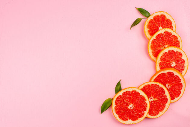 果汁粉红色表面上美味的葡萄柚和多汁的水果片的俯视图美味新鲜切片