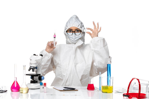 正面前视图身着特殊防护服的女化学家在浅白色背景的covid化学病毒实验室中处理溶液和注射液工作白色光