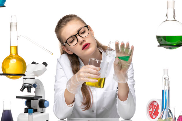 混合前视图穿着医疗服的女化学家在白色背景上混合不同的溶液化学大流行健康病毒健康医疗成人