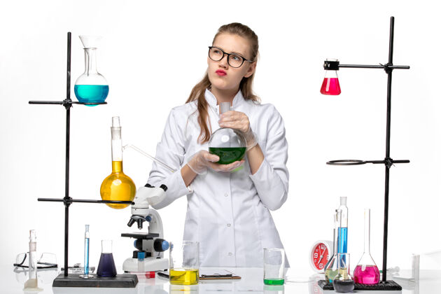 化学前视图穿着医疗服的女化学家拿着装有绿色溶液的烧瓶在白色背景上化学大流行的病毒观点绿色前面