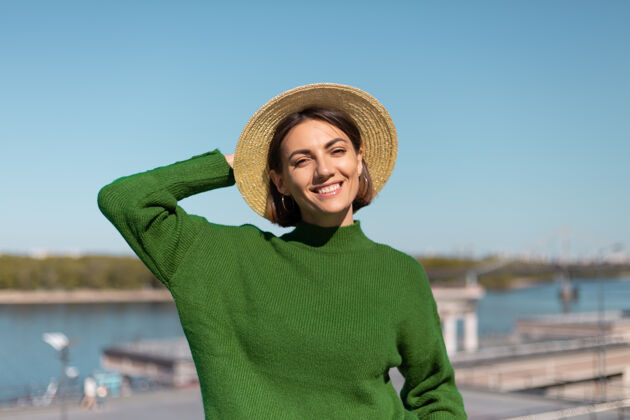 旅游穿着绿色休闲毛衣 戴着帽子的时尚女士在户外的桥上欣赏河景 享受夏日阳光明媚的日子欢乐蓝色旅游