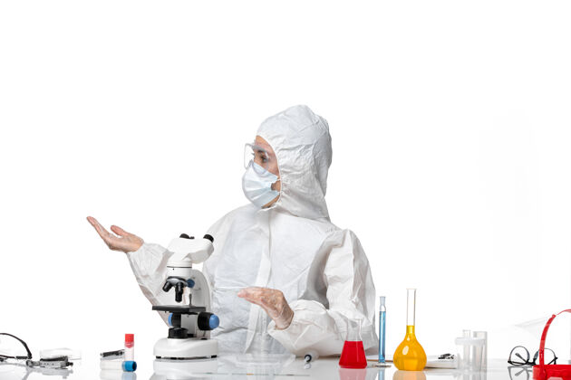 面具前视图：女医生穿着防护服 戴着口罩 因为在白色地板上用显微镜观察病毒大流行 溅出病毒大流行正面成人