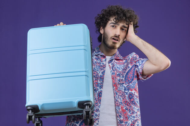 手提箱焦急的年轻英俊的卷发旅行者手举手提箱在孤立的紫色空间年轻紫色卷发