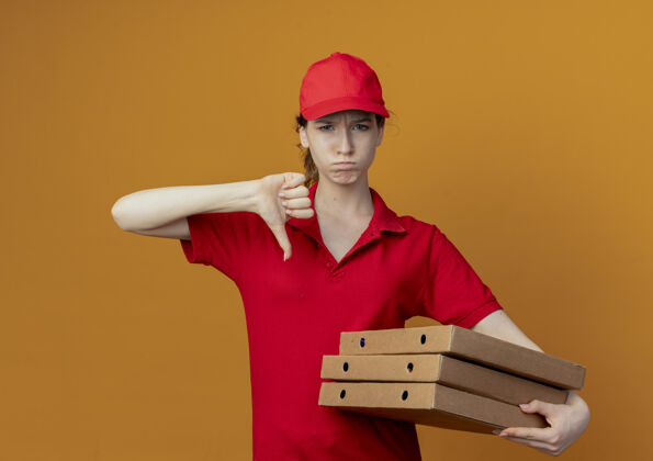 女孩年轻漂亮的送货女孩 穿着红色制服 戴着帽子 手里拿着披萨包 拇指朝下 孤立地站在橙色的背景上拇指橙色披萨