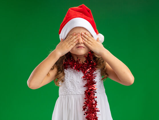 脖子小女孩戴着圣诞帽 脖子上戴着花环 眼睛被遮住 手被隔离在绿色的背景上手帽子盖