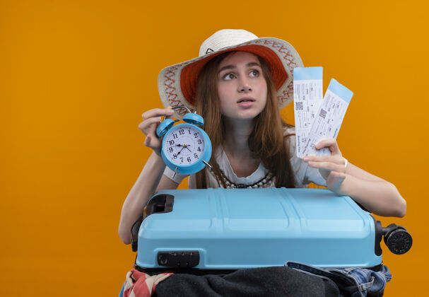 手提箱焦急的年轻旅客女孩拿着机票和闹钟和手提箱在孤立的橙色空间与复印空间机票时钟女孩