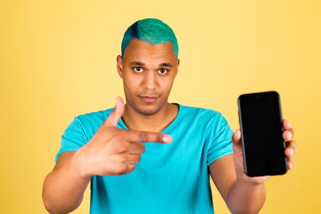 屏幕黑人非洲男人在休闲的黄色墙上用手机积极的快乐点食指在黑色的空屏幕上手机举行设备