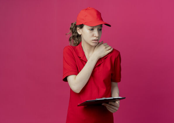 年轻穿着红色制服 戴着帽子的年轻漂亮的送货女孩 手放在肩膀上 手放在肩膀上 红色背景上 留有复印空间举行制服背景