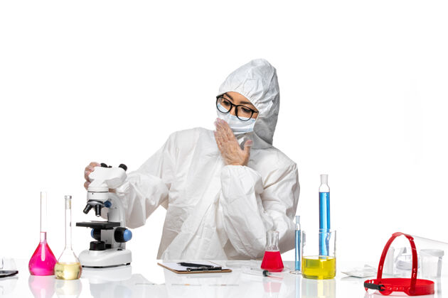 健康前视图穿着特殊防护服的女化学家在白色背景上用显微镜检查样本化学冠状病毒-健康病毒显微镜人检查