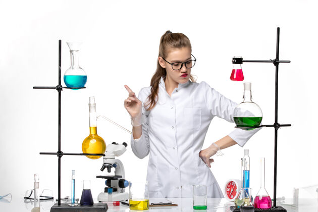 女化学家正面图：身着医疗服的女化学家在工作过程中用白色办公桌上的溶液化学大流行病毒人工作药