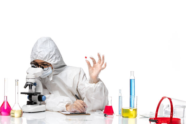 工作正面图穿着特殊防护服的女化学家正在检查白桌子上的样本病毒化学疫苗大流行健康医生样本健康