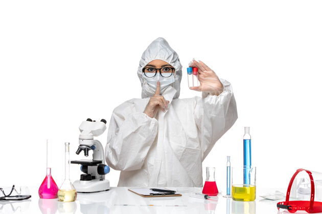 前面正面图穿着特殊防护服的女化学家拿着空瓶子坐在白色的桌子上健康病毒化学健康女化学家化学