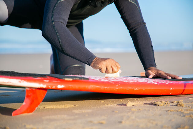 海男冲浪者穿着泳衣在沙滩上给冲浪板打蜡海洋水休闲