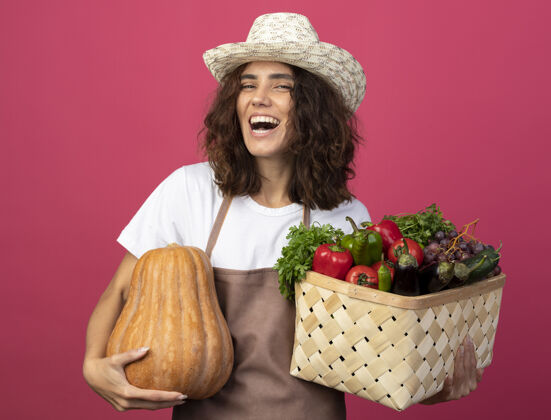 篮子一个年轻的女园丁 穿着制服 戴着园艺帽 手里拿着一个蔬菜篮子 篮子里的南瓜是粉红色的帽子粉色女性