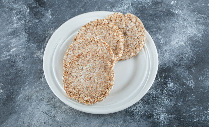 圆一个白色的盘子 上面放满了米粉面包 放在大理石的表面上圆饮食谷类食品