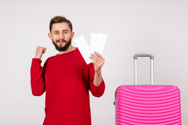 年轻男性正面图年轻男子手拿粉红包 手持机票上白墙航程彩色旅游度假情感照航班男人肤色