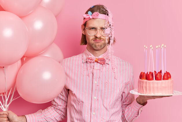 心烦不开心的生日照片派对上心情不好的家伙拿着美味的蛋糕和一堆氦气球蝴蝶结周年纪念脸