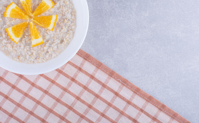 毛巾一盘燕麦片 上面放着橘子片 放在大理石表面橘子健康拼盘