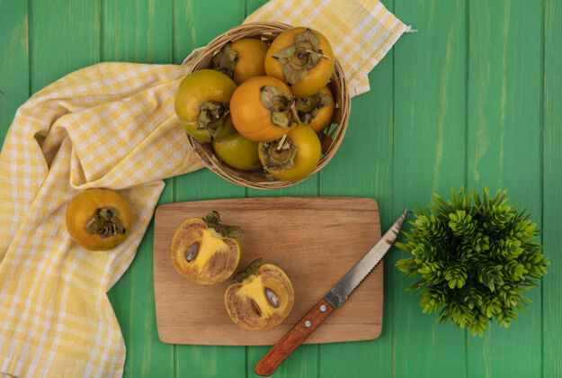 橘子顶视图橙色圆润的柿子水果放在桶上 柿子水果被切成两半放在木制的厨房板上 刀子放在绿色的木桌上顶部厨房视野