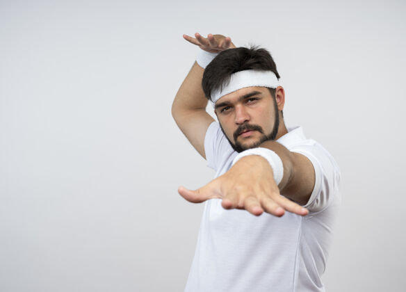 手戴着头带和腕带的自信的年轻运动型男子伸出手 隔离在白色墙壁上 留有复制空间手握腕带佩戴