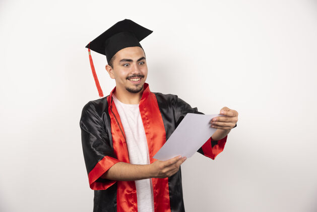 年轻年轻的研究生正高兴地看着白色的毕业证书学生证书长袍