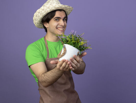 男人微笑着的年轻男园丁穿着制服 戴着园艺帽 在花盆里捧着花花园男人花