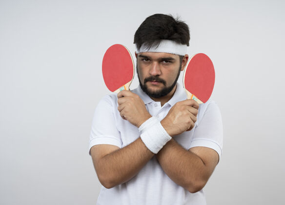 抱着自信的年轻人 戴着头带和腕带 手拿乒乓球拍 隔着白色的墙壁腕带球拍穿
