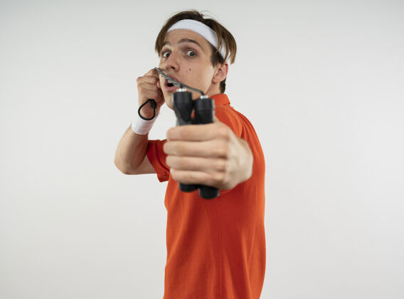 运动型年轻的运动型家伙戴着头带和腕带伸展跳绳隔离在白色墙壁与复制空间戴年轻伸展