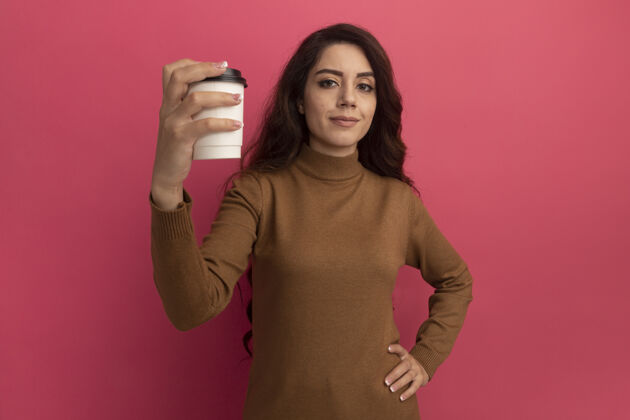 高领毛衣自信的年轻漂亮女孩穿着高领毛衣捧着一杯咖啡孤立在粉红色的墙上咖啡年轻穿