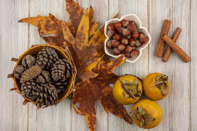 桂皮顶视图松果桶上的叶子与榛子在一个碗肉桂棒在一个灰色的木桌上锥叶秋