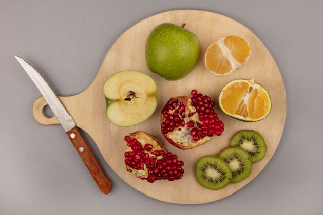 橘子美味的切片猕猴桃与苹果橘子和石榴在木制菜板与刀的俯视图灰色顶部厨房
