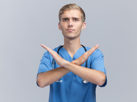 男性严格的年轻男医生穿着医生制服 听诊器显示没有孤立的姿态在白墙上听诊器制服年轻
