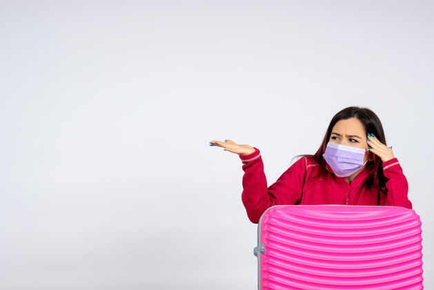 病毒正面图年轻女性带着粉红色的袋子在白墙上戴着口罩度假病毒covid-彩色旅行女性大流行微笑游客女人