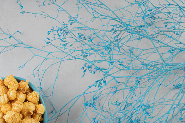 美学蓝色的一碗焦糖味爆米花 旁边是大理石背景上的装饰树枝小吃焦糖碗