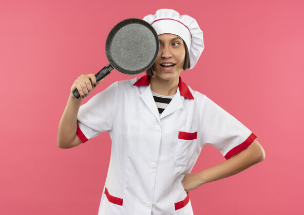 薯条快乐的年轻女厨师穿着厨师制服 手里拿着一只粉红色的煎锅烹饪厨师快乐