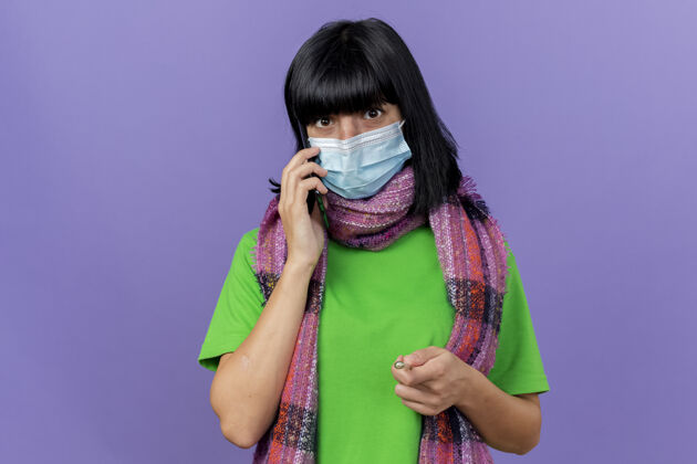公民印象深刻的年轻生病的女人戴着口罩和围巾看着前面讲电话隔离在紫色墙上的复制空间衣服印象疾病
